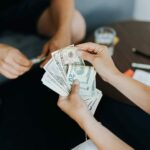 Close-up of people handling and counting US dollar bills indoors.